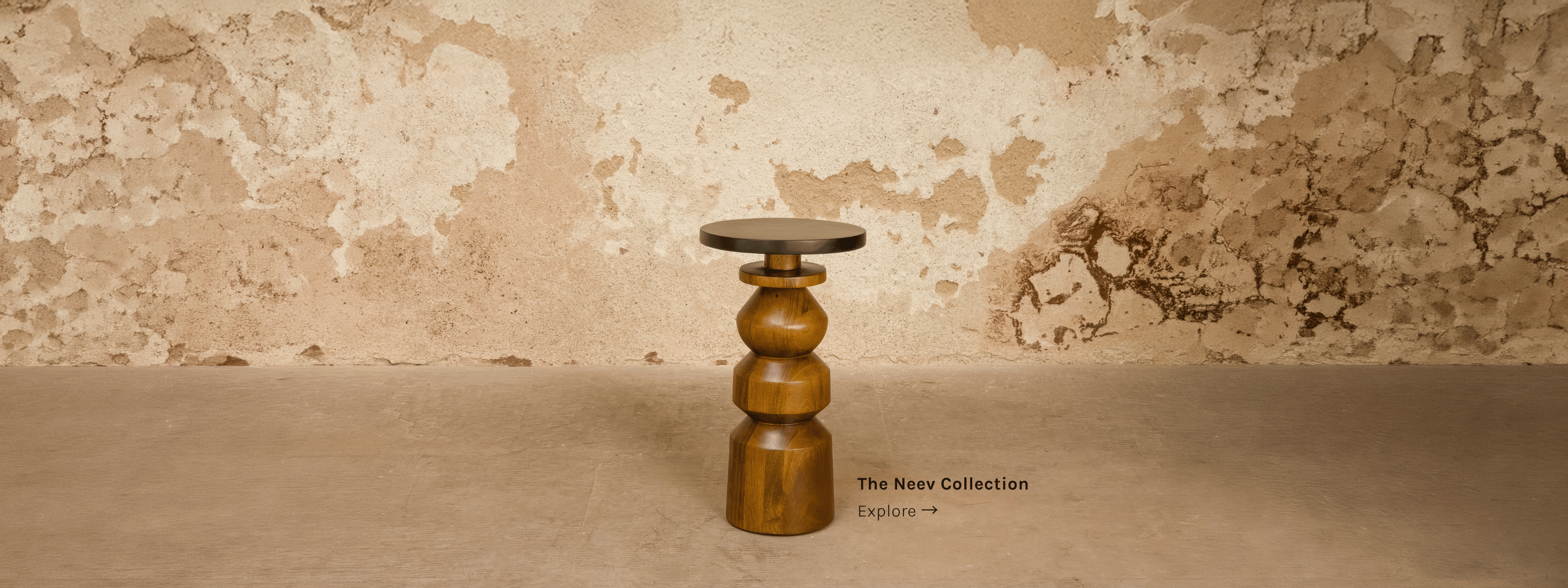 Gubbi turned-wood end table from the Neev Collection by India Design House, against a weathered plaster wall