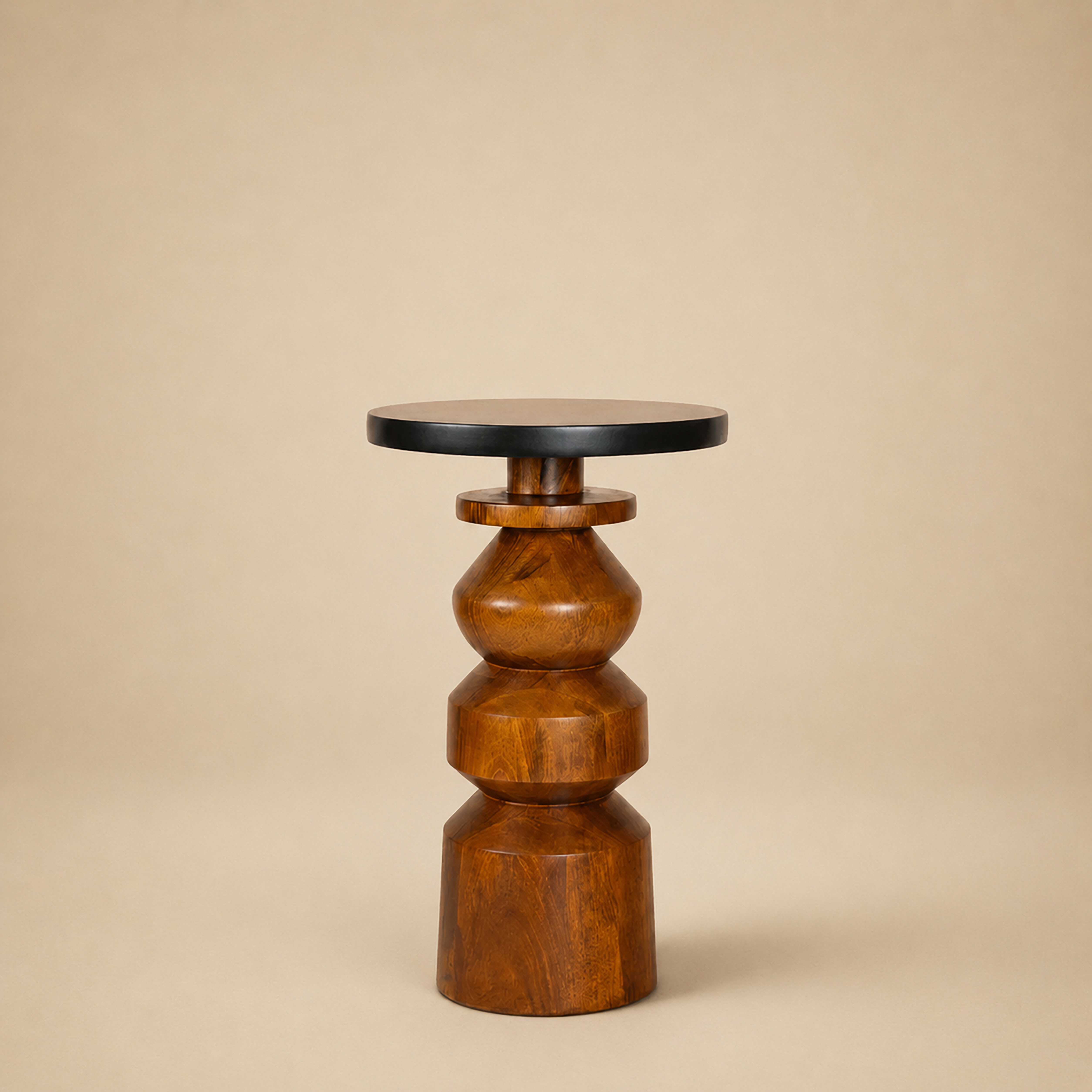 Gubbi end table with a stacked lathe-turned wood base and round black top, on a neutral backdrop